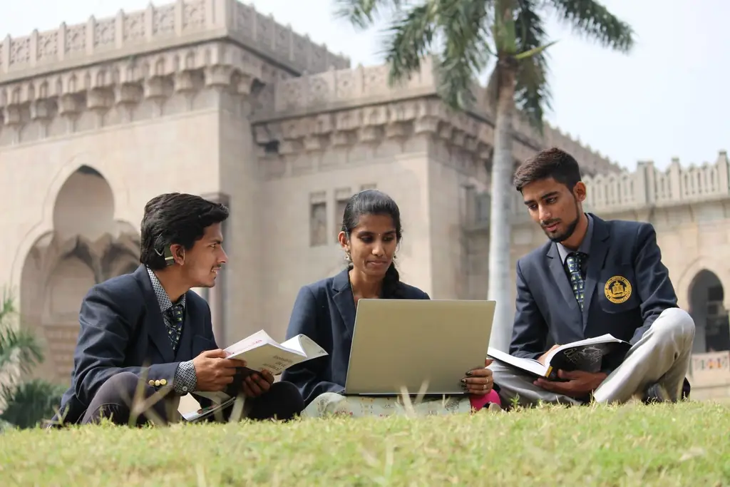 Three students studying together on a lawn outside a historic university building