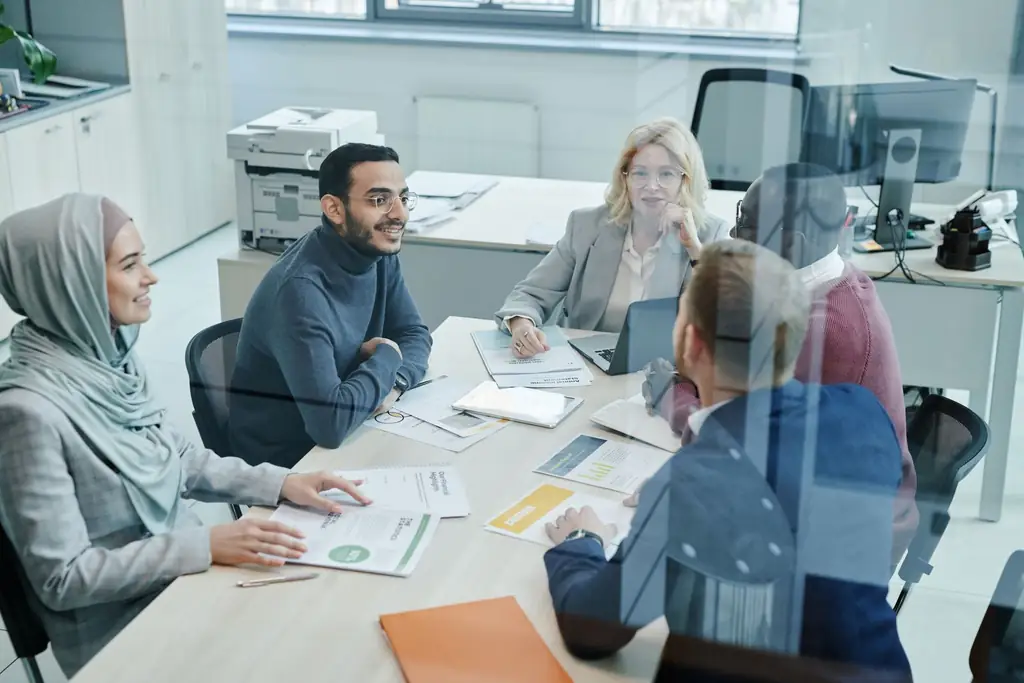 Colleagues discussing documents around a table in an open-plan office