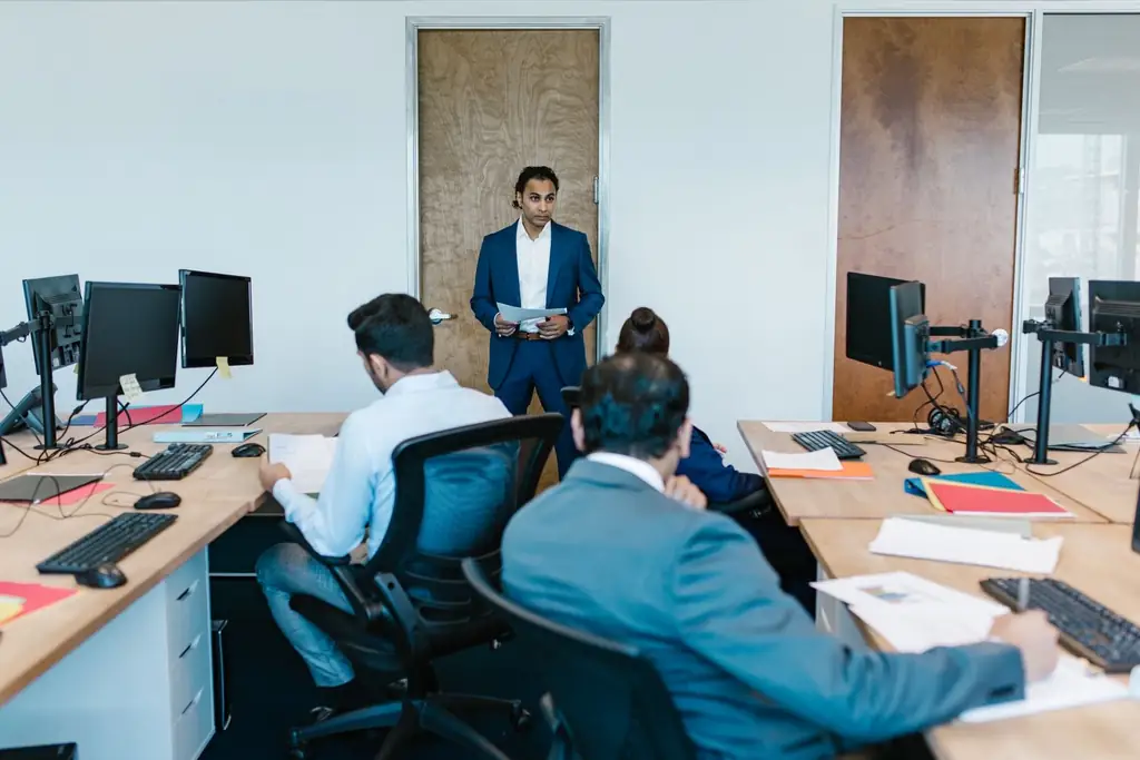 A manager presenting to colleagues at their desks in an open-plan office